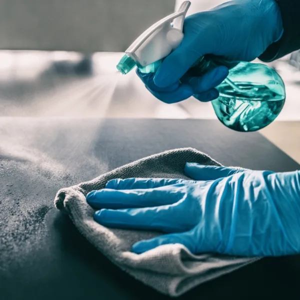 Gloved hands diligently spray and wipe a surface, ensuring the service areas are impeccably clean.
