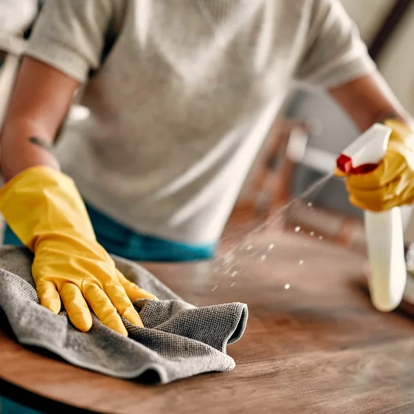 Wearing yellow gloves, a person methodically applies cleaning services to a wooden surface, skillfully using a spray bottle and cloth.