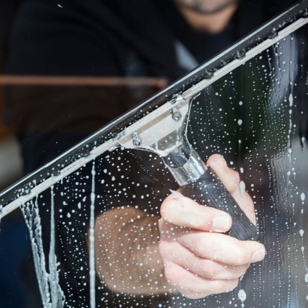A person efficiently uses a squeegee to provide exceptional cleaning services, leaving the soapy window spotless.