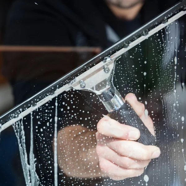A person efficiently uses a squeegee to provide exceptional cleaning services, leaving the soapy window spotless.