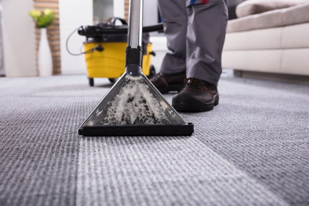 A person providing residential cleaning services in a living room carpet a fresh makeover with a steam cleaner. The home feels renewed, as the yellow cleaning machine hums gently nearby.