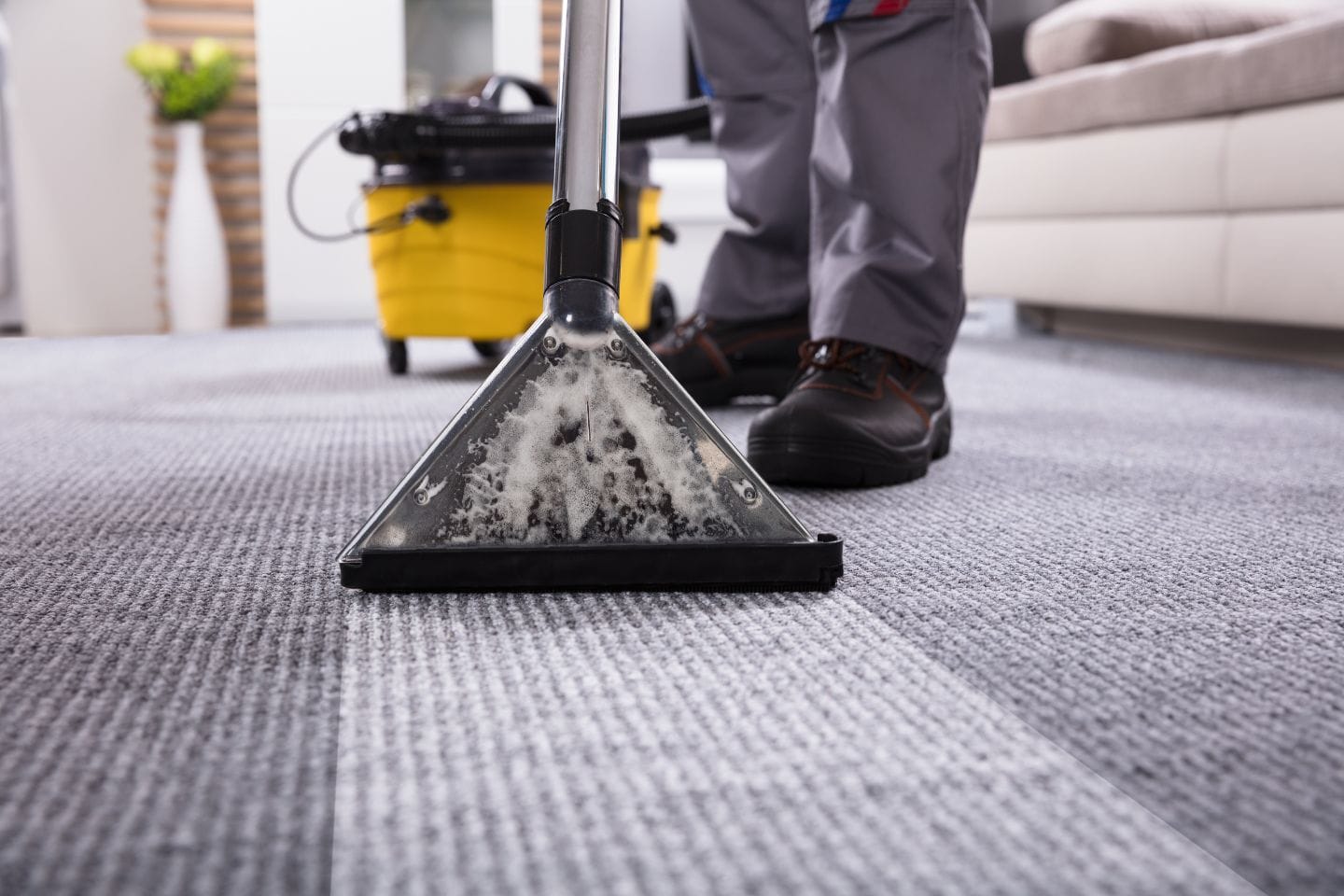 A person providing residential cleaning services in a living room carpet a fresh makeover with a steam cleaner. The home feels renewed, as the yellow cleaning machine hums gently nearby.