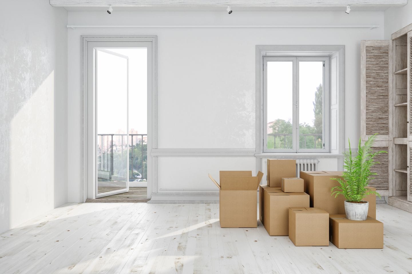 A bright, empty room with large windows, boxes, and a potted plant on the floor suggests it's ready for move-out cleaning. One window is open to a small balcony, inviting fresh air ahead of its next chapter.
