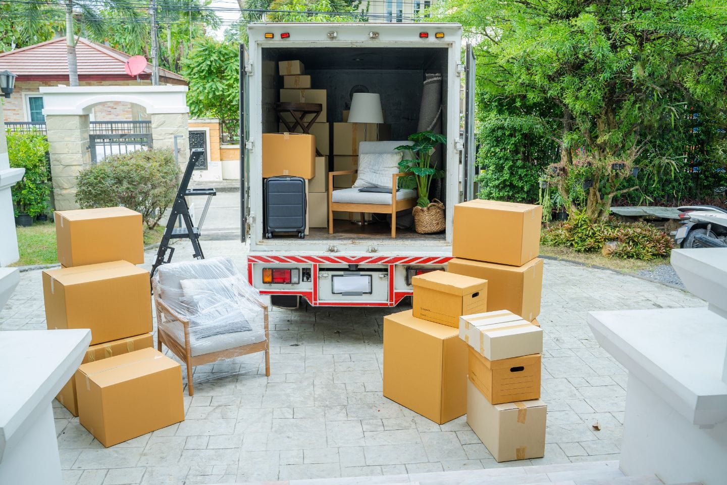 A moving truck filled with furniture and boxes is parked in a driveway surrounded by additional cardboard boxes, ready for the final touch of move-out cleaning. A chair and a suitcase are visible inside the truck, hinting at a fresh start ahead.