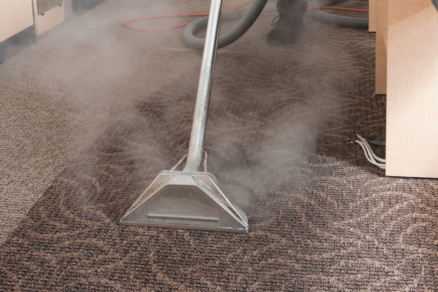 A steam cleaner diligently glides over the patterned office carpet, releasing visible steam and transforming the cleaning process into a seamless task.