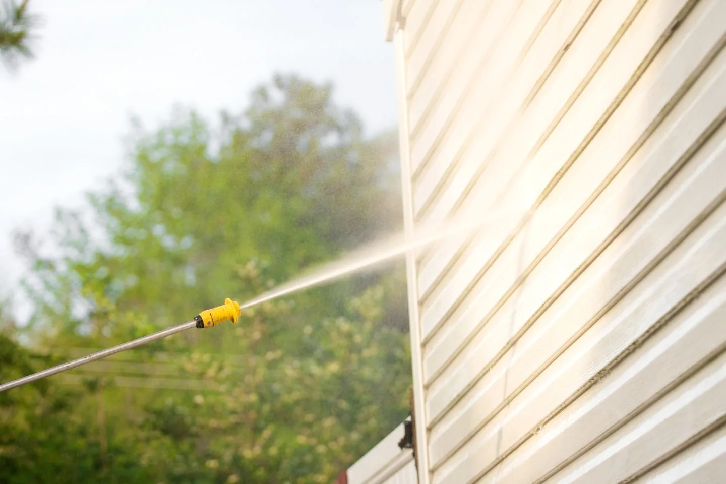 A person is pressure washing the siding of a house.