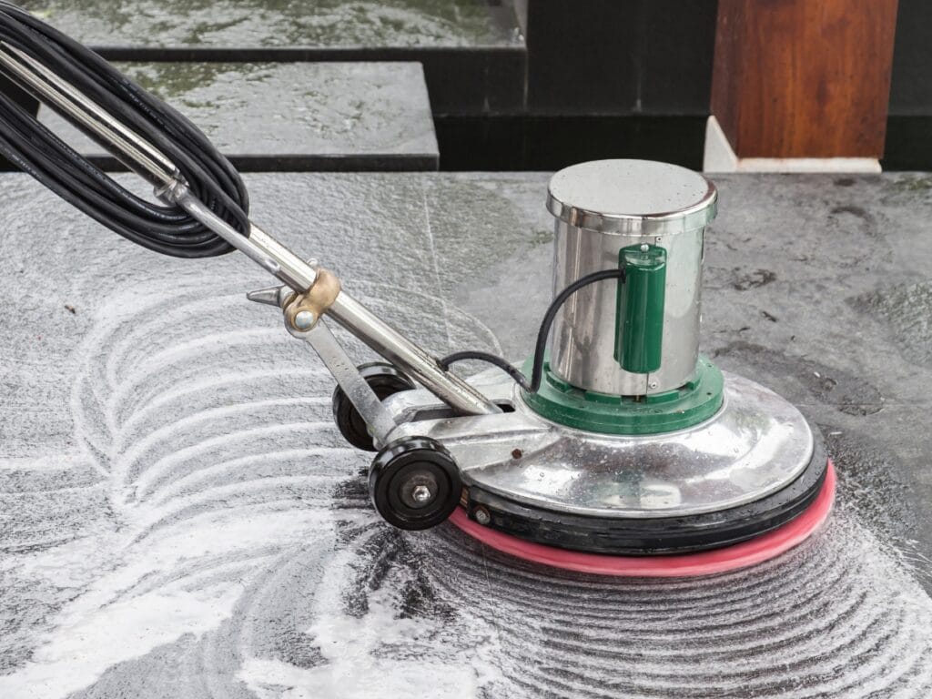 A floor scrubbing machine with a pink brush attachment is cleaning a dirty, soapy tile floor, leaving circular cleaning marks&mdash;ideal preparation before professional Floor Waxing Services.