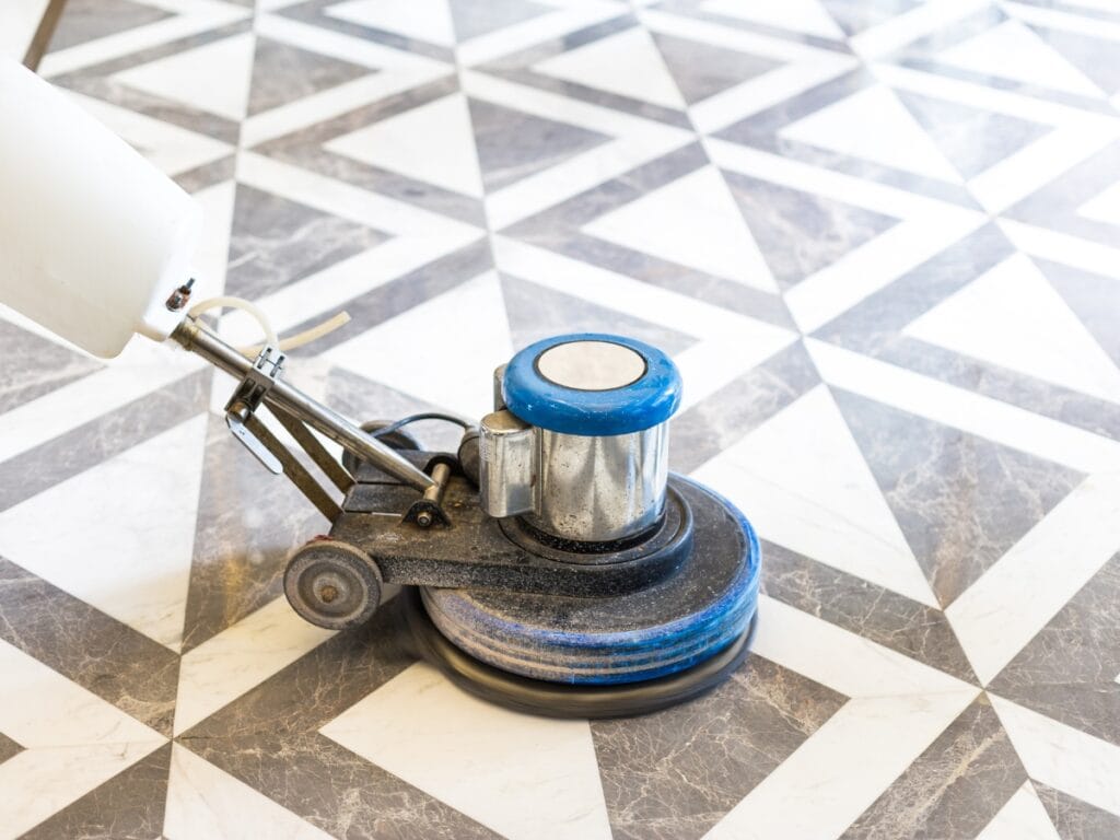 A floor polishing machine in use on a black, white, and gray geometric patterned tile floor, showcasing the professional results of expert Floor Waxing Services.